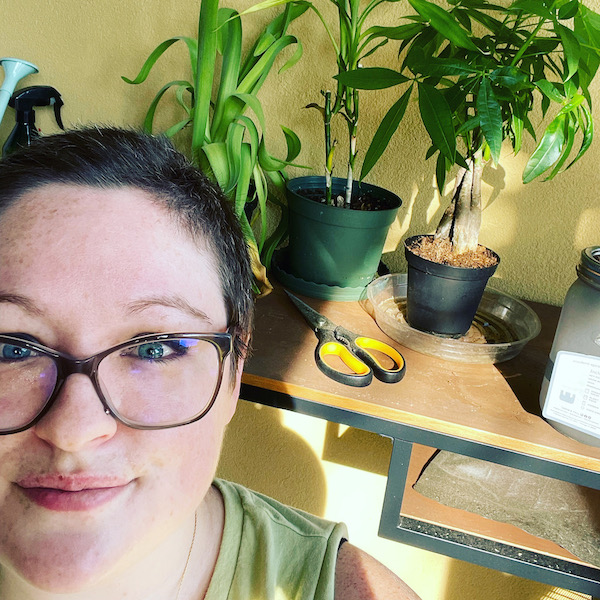 A white genderqueer person standing in front of a table covered with houseplants